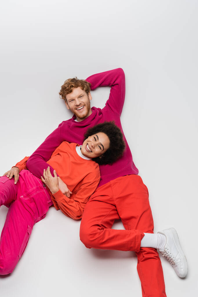 top view of cheerful african american woman resting with redhead man in magenta color clothes on white  - Foto, immagini