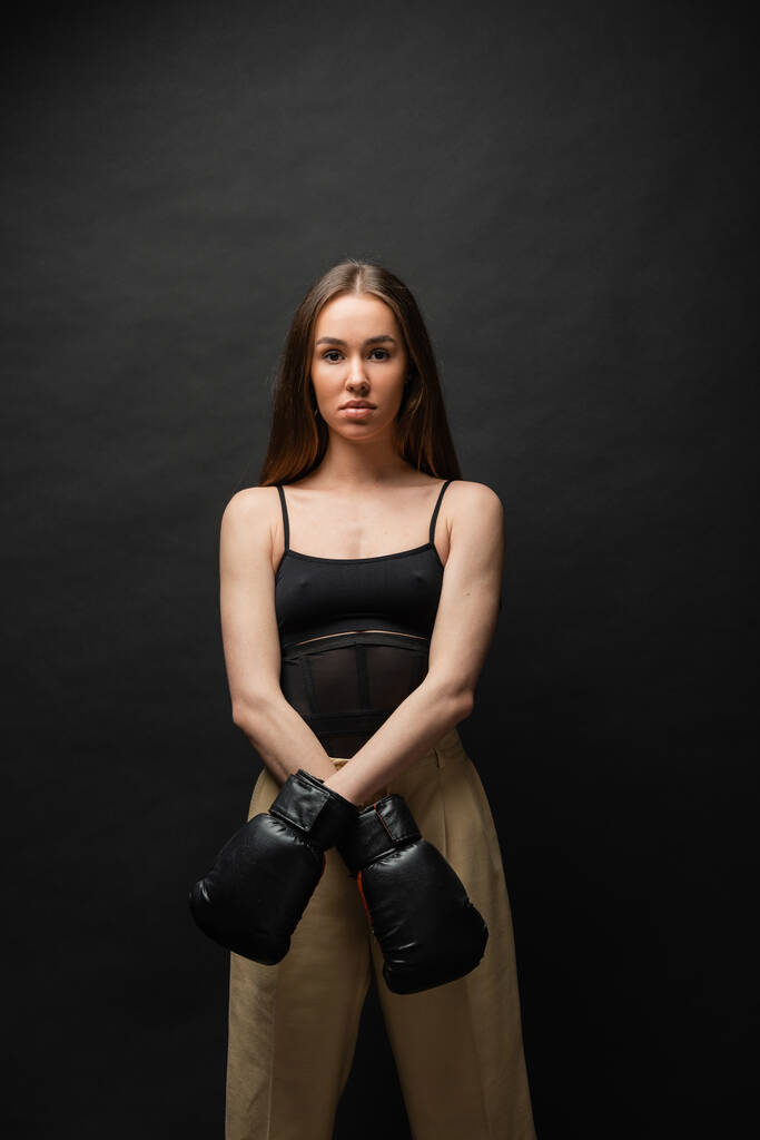 brunette woman in top and beige pants posing in boxing gloves on black background  - Foto, Imagem