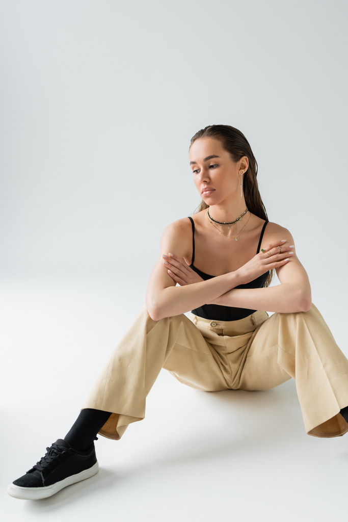 full length of thoughtful woman in beige pants and black top sitting on grey  - Foto, immagini