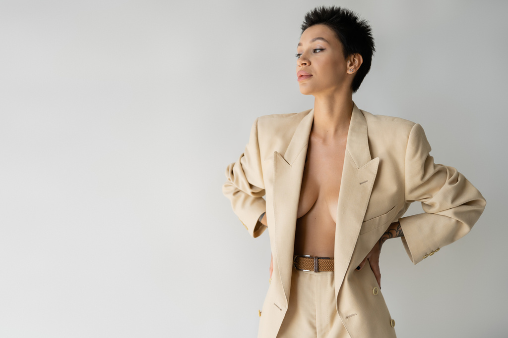 young woman in beige suit on sexy shirtless body standing with hands on waist isolated on grey - Photo, Image