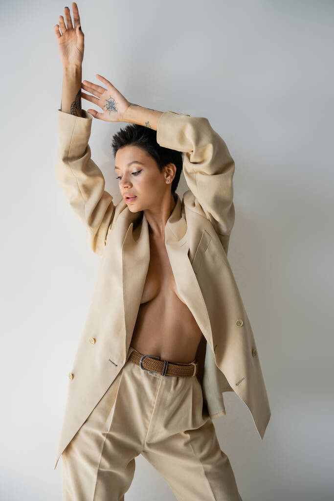 young and sexy woman in beige suit on shirtless body posing with arms up on grey background - Fotografie, Obrázek