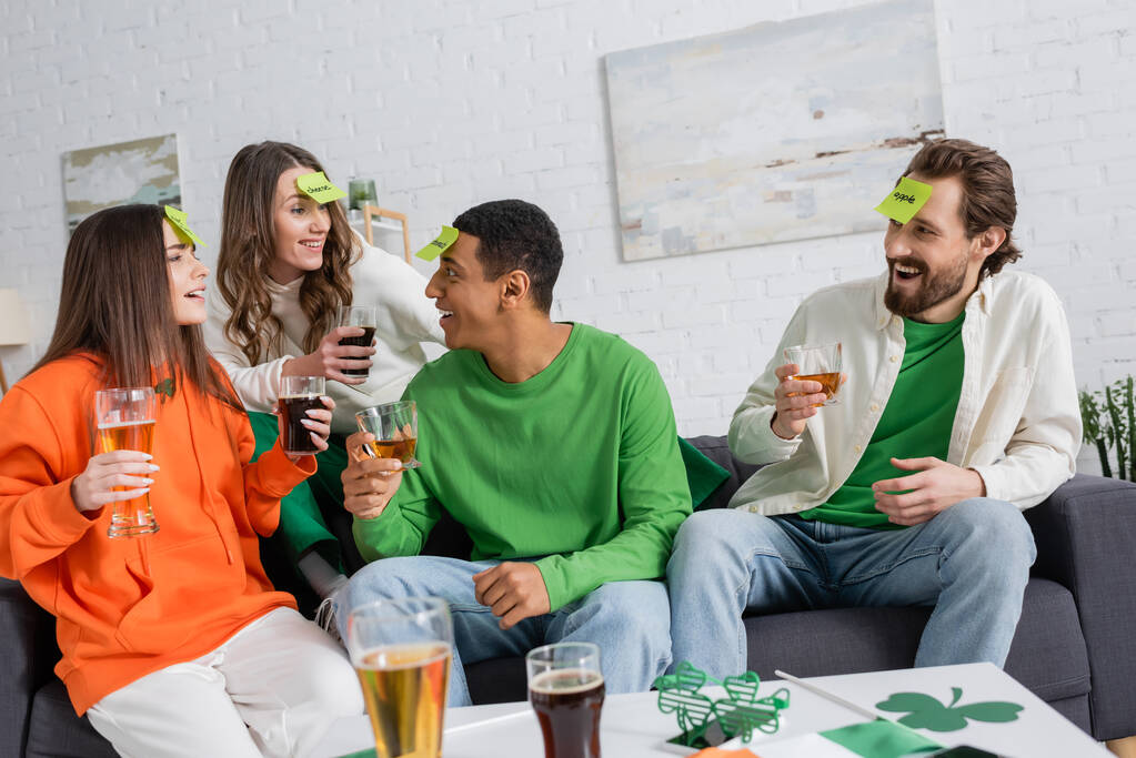 Веселые межрасовые друзья с напитками играют кто я есть игра во время празднования дня святого Патрика  - Фото, изображение