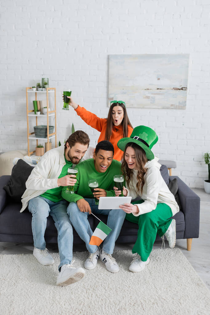 Pozitivní multietnické přátelé se zeleným pivem pomocí digitálního tabletu na gauči doma  - Fotografie, Obrázek