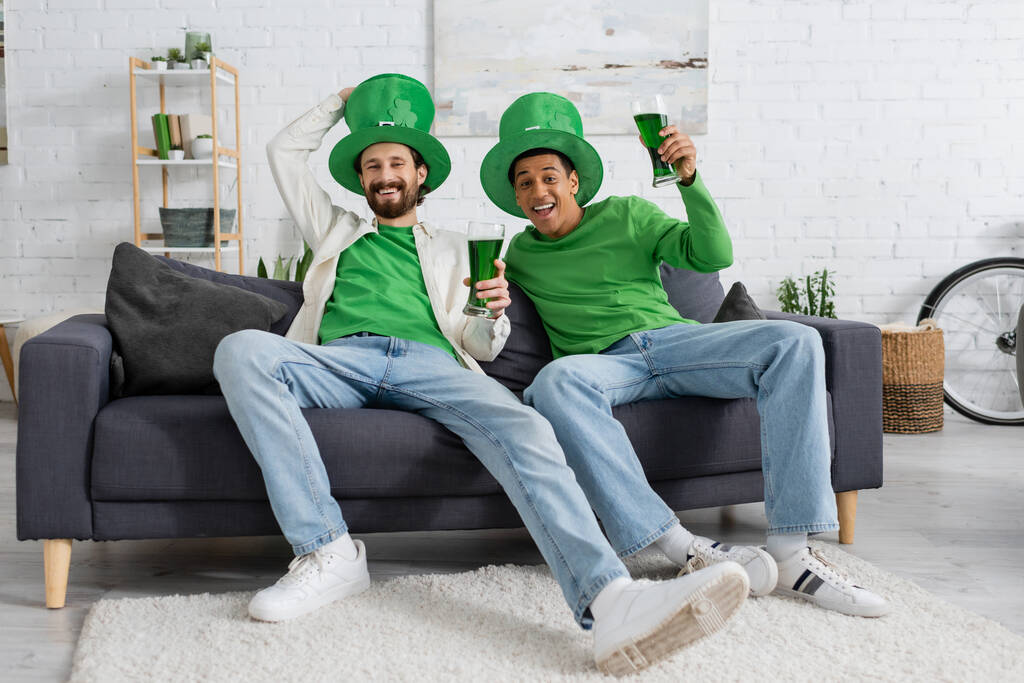 Sonrientes amigos multiétnicos con sombreros festivos sosteniendo cerveza verde mientras celebran el día de San Patricio - Foto, Imagen