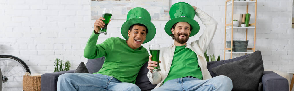 Felices amigos multiétnicos con cerveza verde mirando a la cámara mientras celebran el día de San Patricio, pancarta  - Foto, imagen
