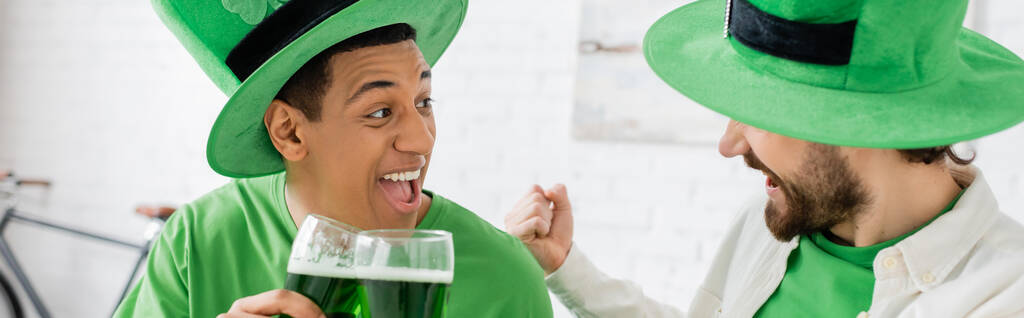 Excited multiethnic men with green beer celebrating saint patrick day at home, banner  - Foto, immagini