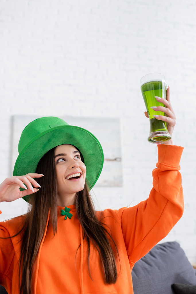Vidám nő zöld kalapban, kezében egy pohár répával a nappaliban.  - Fotó, kép