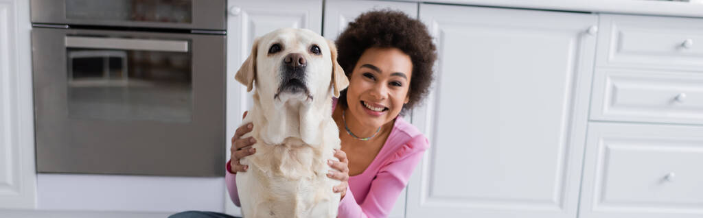 Feliz mulher afro-americana petting labrador na cozinha, banner  - Foto, Imagem
