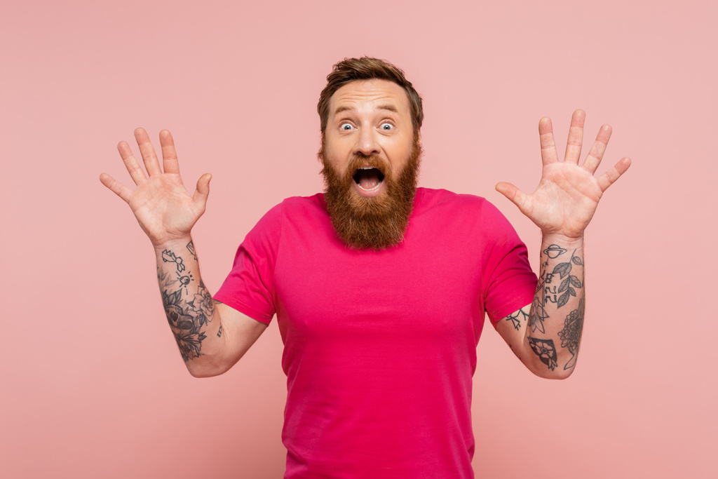 ενθουσιασμένος άνδρας με τατουάζ με ανοιχτό στόμα δείχνει wow χειρονομία και κοιτάζοντας κάμερα απομονωμένη σε ροζ - Φωτογραφία, εικόνα