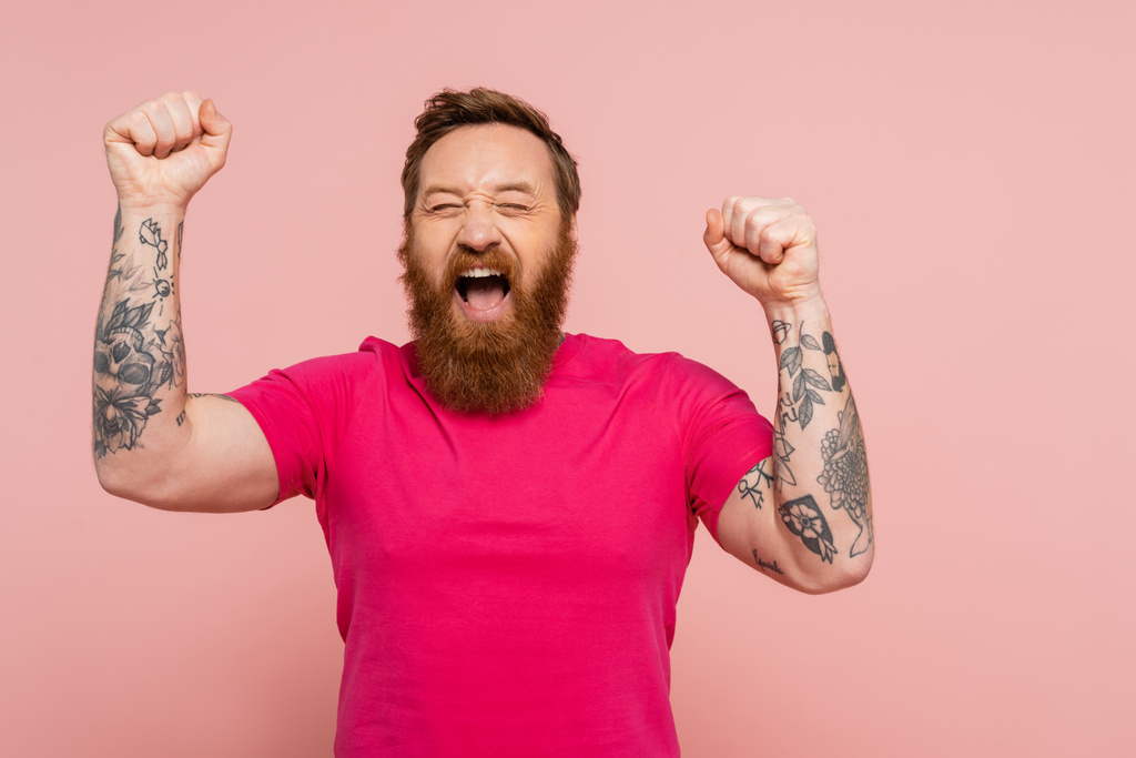 joyful bearded man with closed eyes showing triumph gesture and screaming isolated on pink - Fotografie, Obrázek