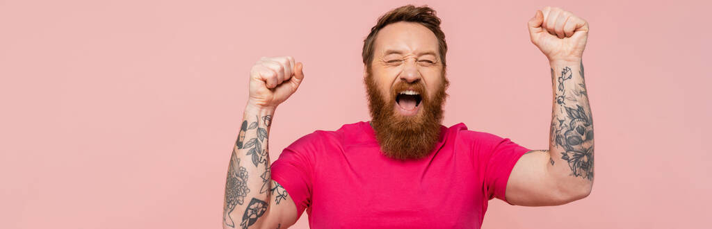 eccitato uomo tatuato con gli occhi chiusi gridando e mostrando vincere gesto isolato su rosa, banner - Foto, immagini