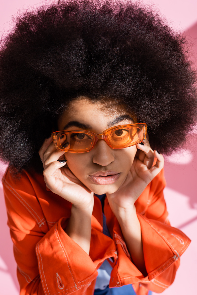 Kıvırcık, turuncu güneş gözlüklü, pembe kameraya bakan Afro-Amerikan kadın manzarası.  - Fotoğraf, Görsel