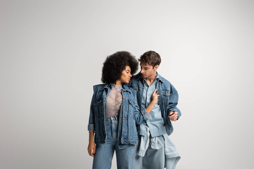 curly african american model touching denim jacket of young man isolated on grey  - Foto, immagini