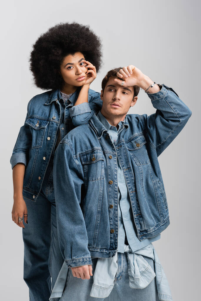 curly african american woman standing with man in denim outfit isolated on grey - Photo, Image
