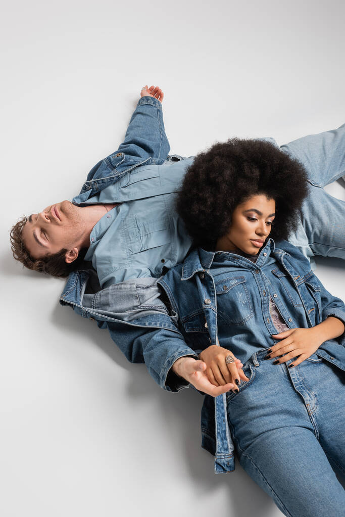 high angle view of african american woman leaning on man in denim clothes lying on grey  - Fotografie, Obrázek