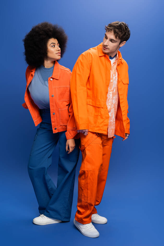 Interracial models in jackets looking at each other on blue background - Photo, Image