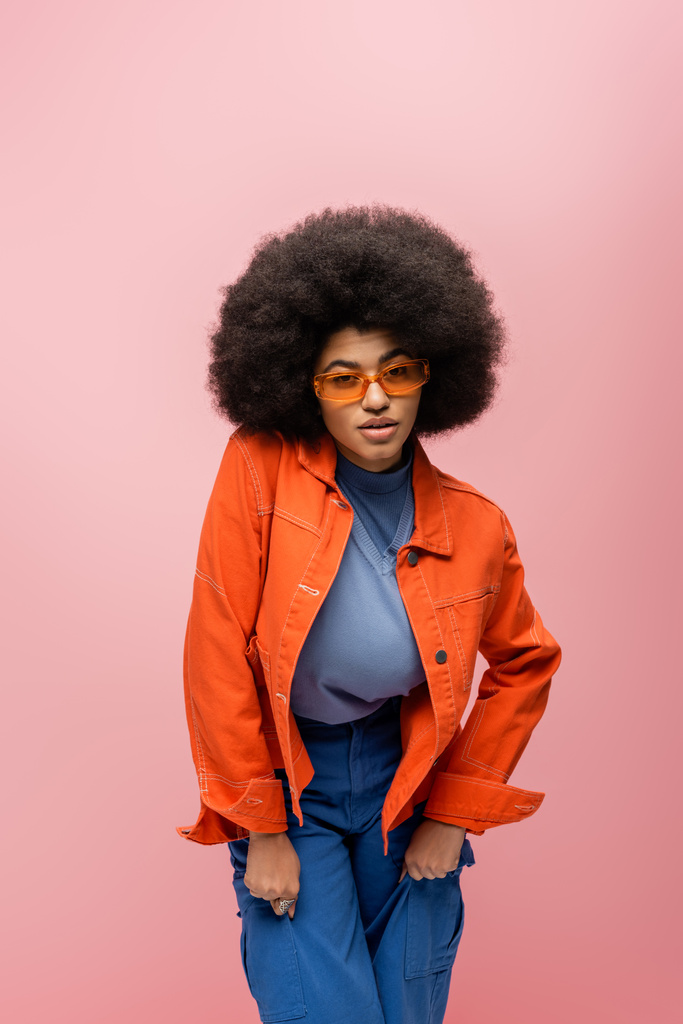 Afroamerikanerin mit Sonnenbrille und hellem Outfit isoliert auf rosa  - Foto, Bild