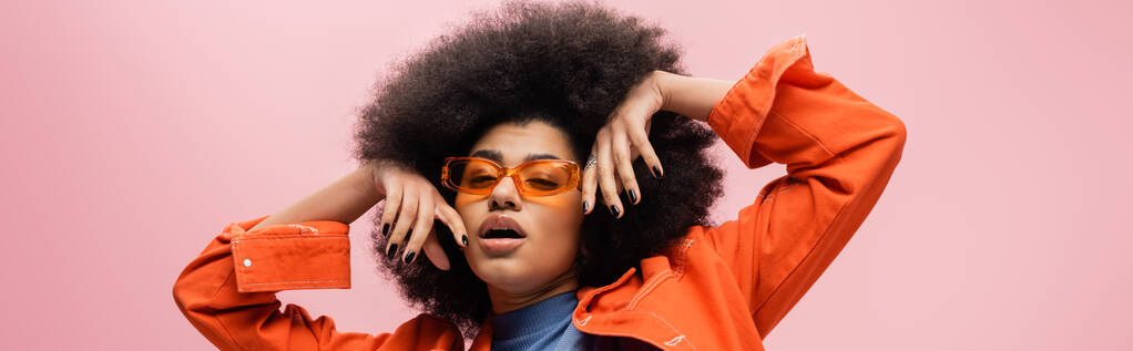 Elegante modello afroamericano in giacca arancione e occhiali da sole isolati su rosa, banner  - Foto, immagini