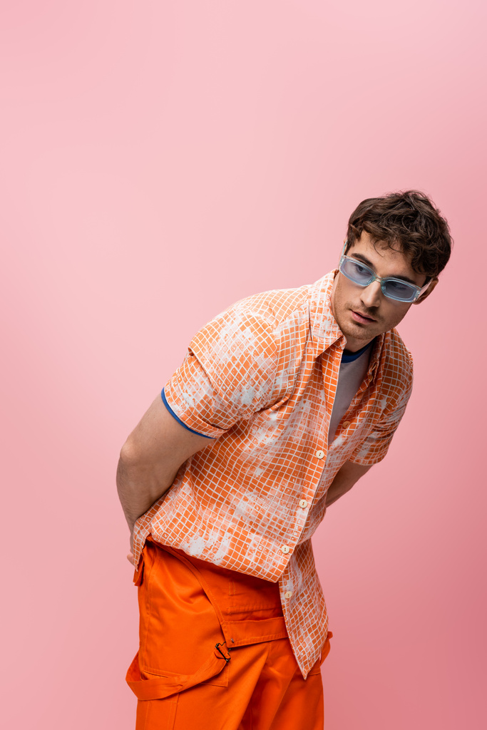 Young brunette man in sunglasses and shirt looking away isolated on pink  - Photo, Image