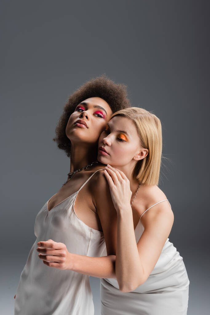 brunette african american woman in white camisole looking away near young blonde model isolated on grey - Fotografie, Obrázek