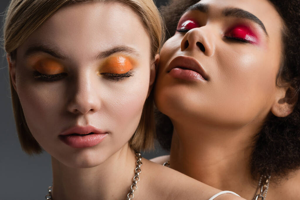 portrait of sensual multiethnic models with bright and glossy eye shadows isolated on grey - Photo, Image