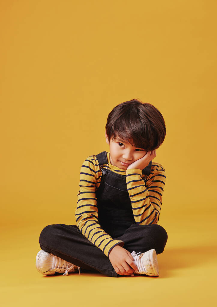 One asian boy looking sad and depressed while sitting on the floor and posing against orange copyspace background. Cute mixed race child with ADD looking bored and depressed. - Foto, Imagem