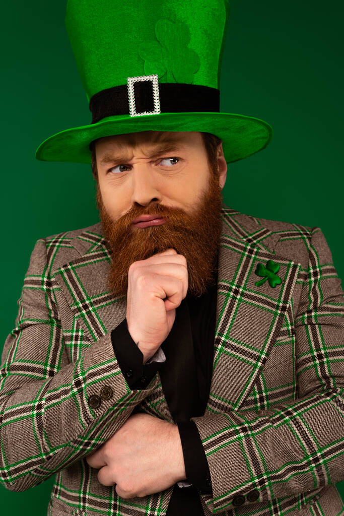 Pensivo barbudo homem de chapéu com trevo olhando para longe isolado em verde  - Foto, Imagem