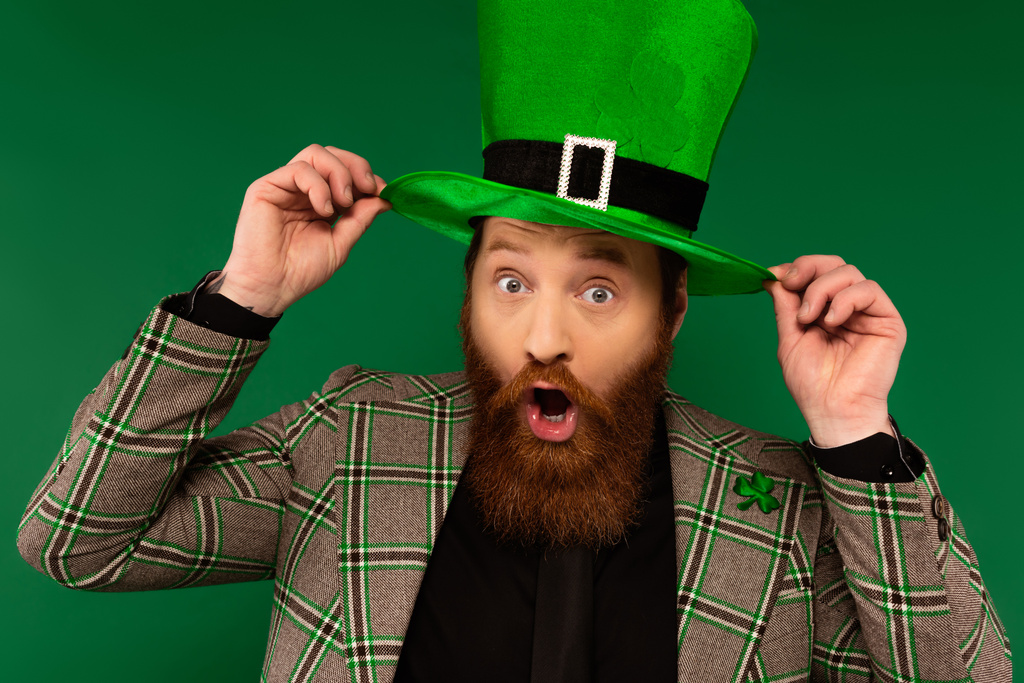 Sorprendido hombre barbudo con sombrero con trébol aislado en verde  - Foto, Imagen