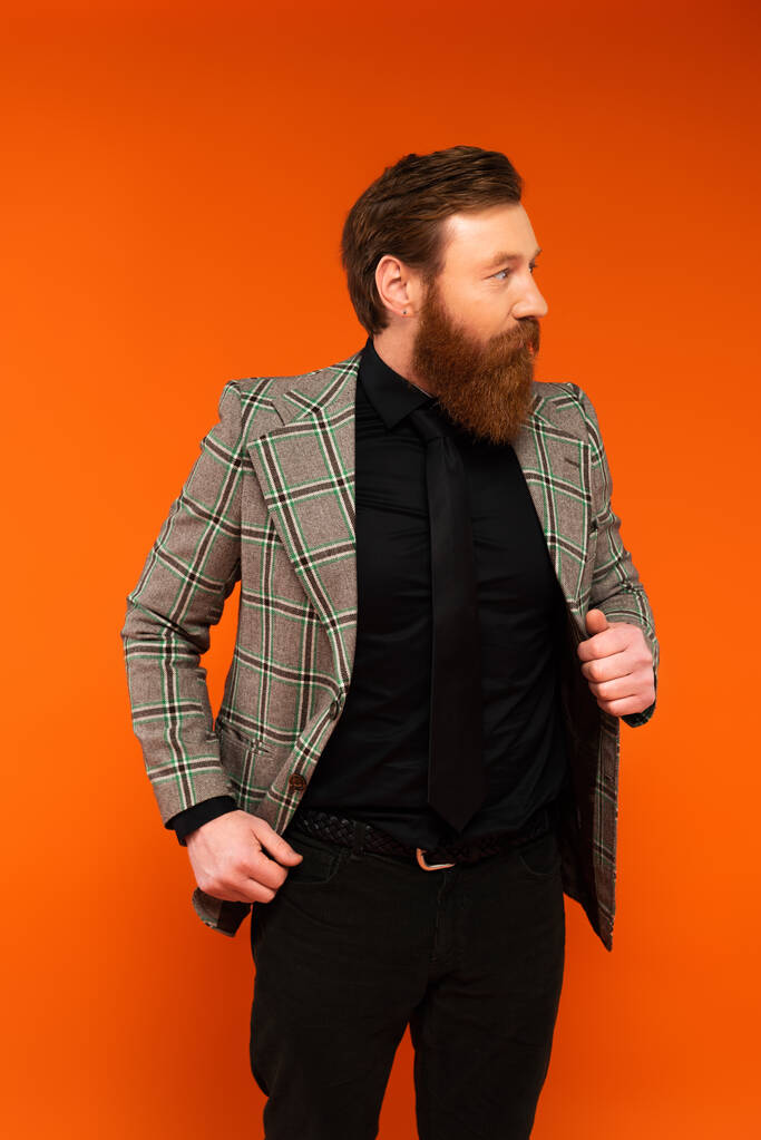 Стильний бородатий чоловік у плетеній куртці дивиться ізольовано на червоному
  - Фото, зображення