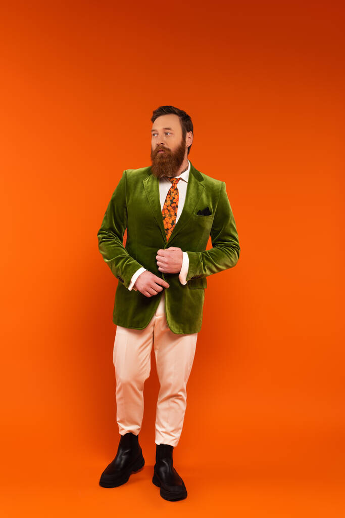 Volledige lengte van trendy man met baard verstelbare jas op rode achtergrond  - Foto, afbeelding