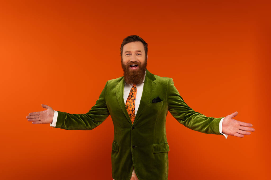 Cheerful bearded man in velvet jacket looking at camera isolated on red  - Foto, afbeelding