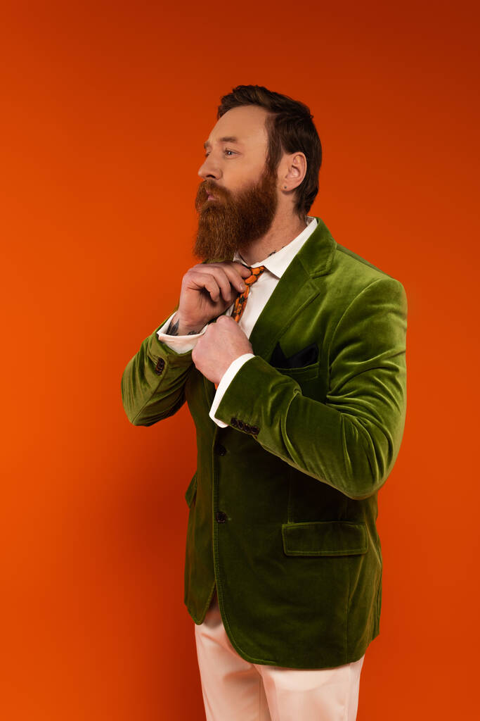 Fashionable bearded man adjusting tie isolated on red  - Zdjęcie, obraz