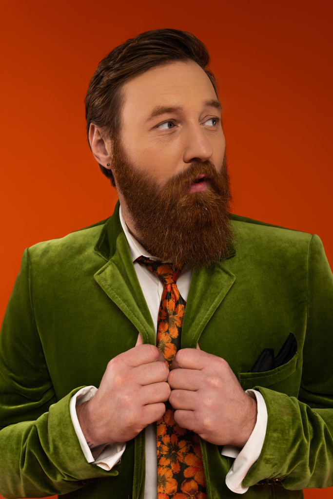 Trendy man met baard in fluwelen jasje op zoek weg geïsoleerd op rood  - Foto, afbeelding