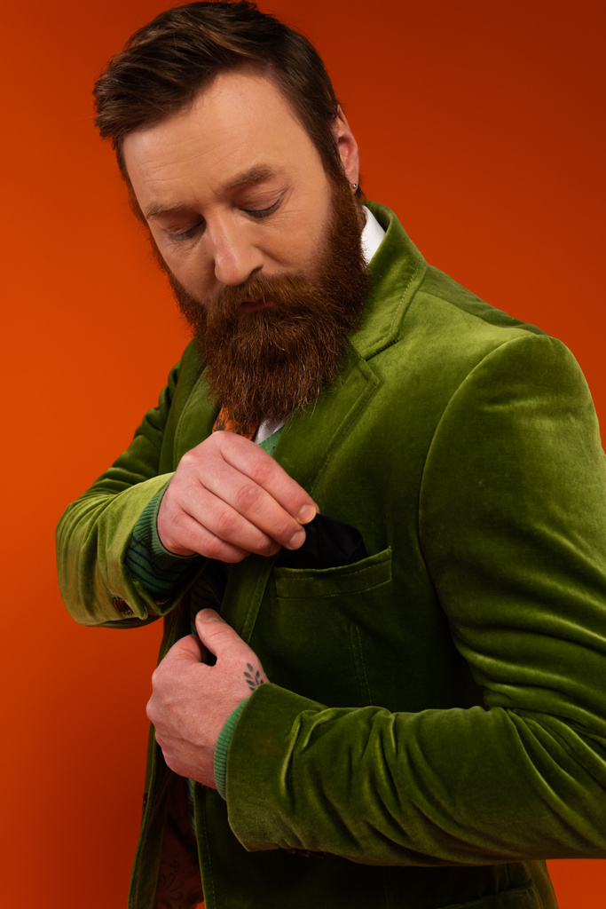 Portrait de modèle tatoué mettant mouchoir dans la poche de la veste sur fond rouge  - Photo, image