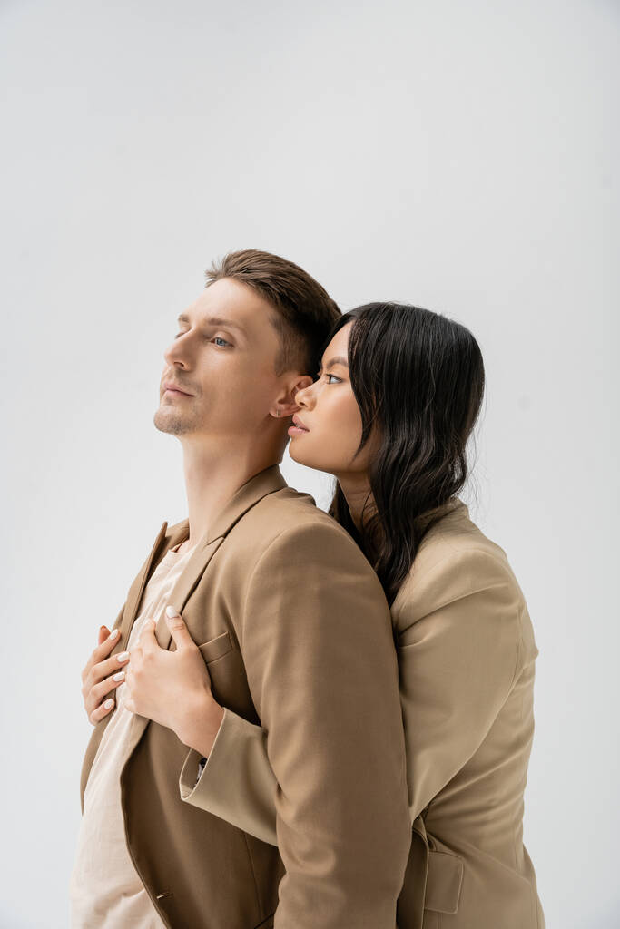 sensual asian woman embracing man in trendy blazer isolated on grey - Photo, Image