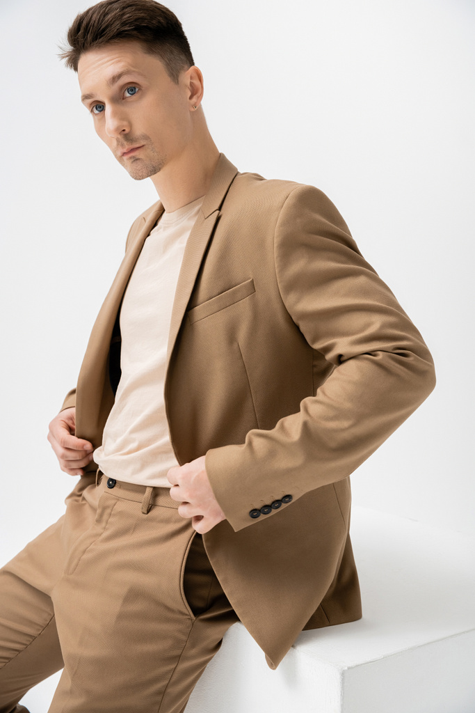 fashionable man in beige stylish suit looking away near cube on white background - Zdjęcie, obraz