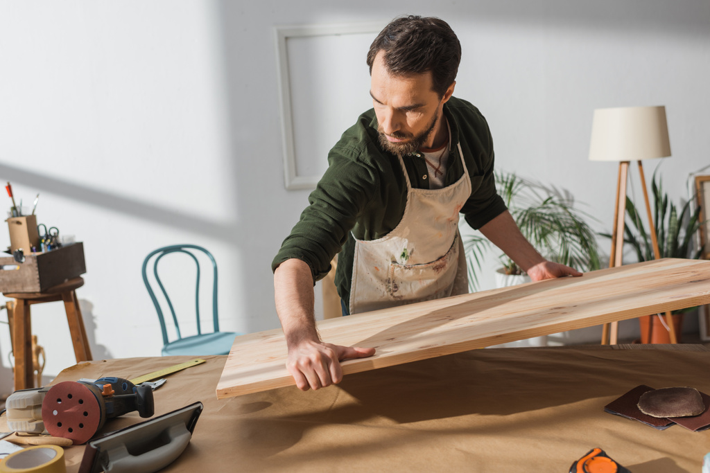 Τεχνίτης που τοποθετεί δασικές σανίδες στο τραπέζι κοντά σε εργαλεία  - Φωτογραφία, εικόνα