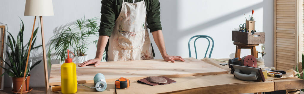 Обрізаний вид ремонтника в фартусі, що стоїть біля дерев'яної дошки та інструментів в майстерні, банер
  - Фото, зображення