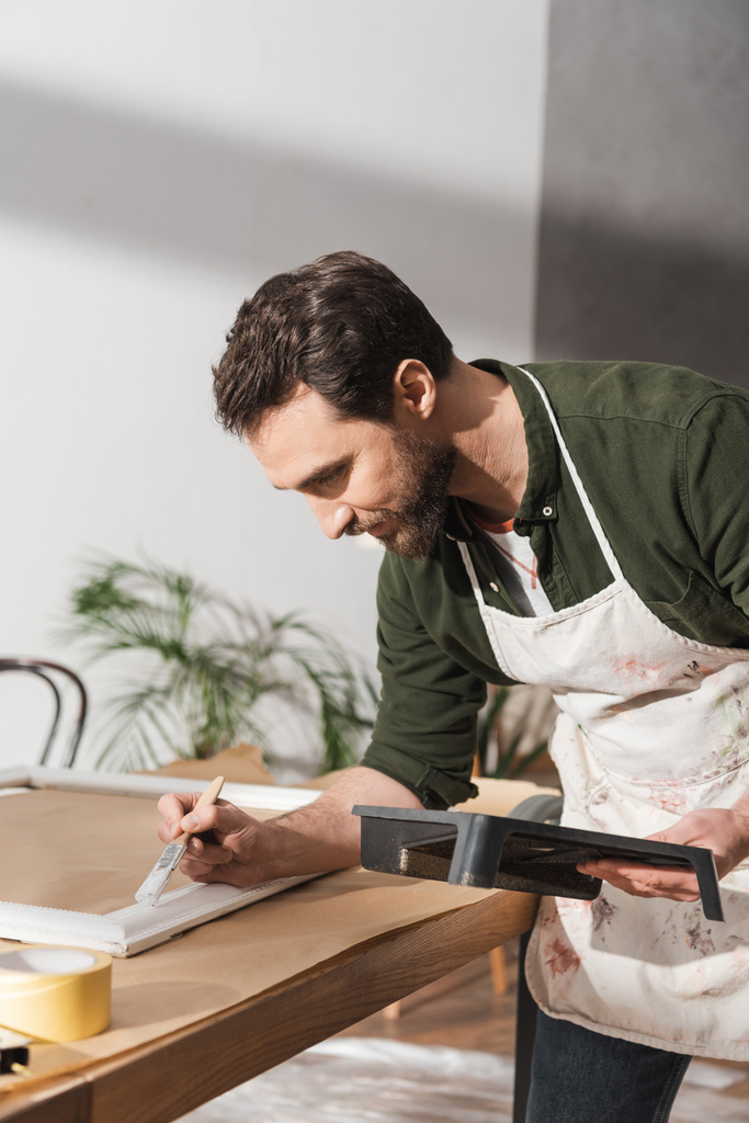 Bearded repairman painting on wooden board in workshop  - Photo, Image