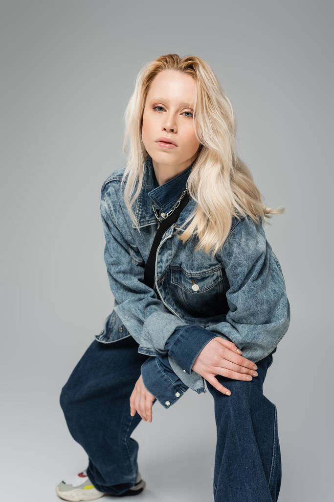 young blonde model in trendy denim outfit looking at camera isolated on grey  - Foto, imagen