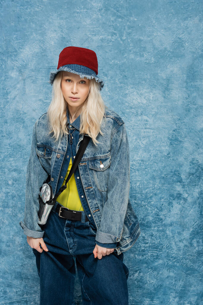 blondýny žena v džínové bundě a panama klobouk úprava trendy džíny v blízkosti modré texturované pozadí   - Fotografie, Obrázek