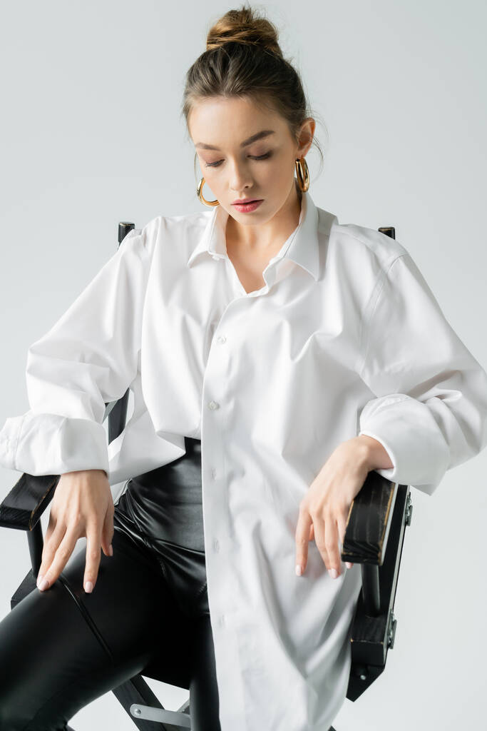 stylish woman sitting on chair in white oversize shirt isolated on grey - Photo, Image