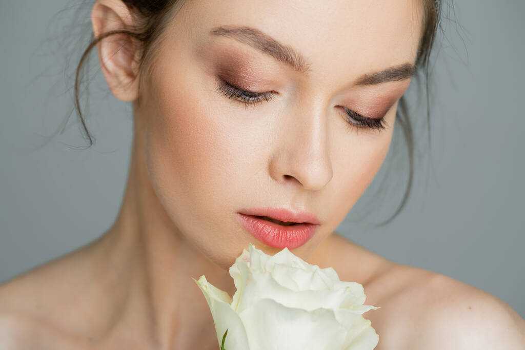 charming woman with clean skin and natural makeup looking at white rose isolated on grey - Foto, Imagem