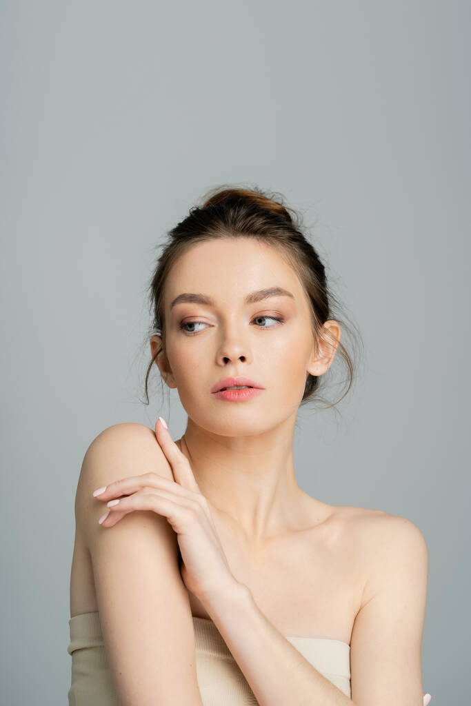 junge Frau mit nackten Schultern und natürlichem Make-up posiert isoliert auf grau - Foto, Bild