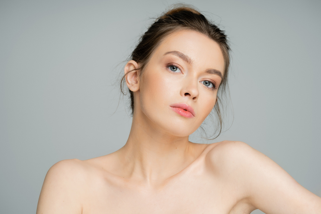 charming woman with natural makeup and naked shoulders looking at camera isolated on grey - Fotoğraf, Görsel