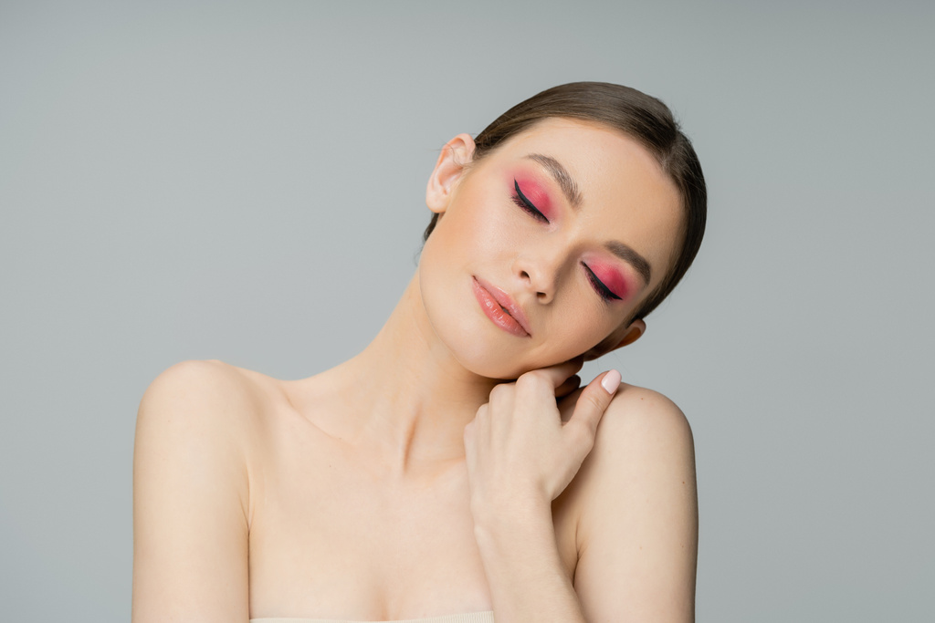 Pretty young model with pink makeup touching shoulder isolated on grey  - Foto, Imagen