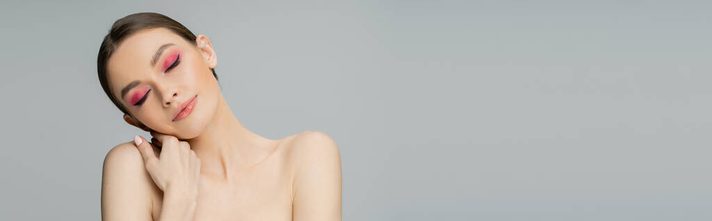 Young woman with bright makeup touching naked shoulder isolated on grey, banner  - Foto, afbeelding