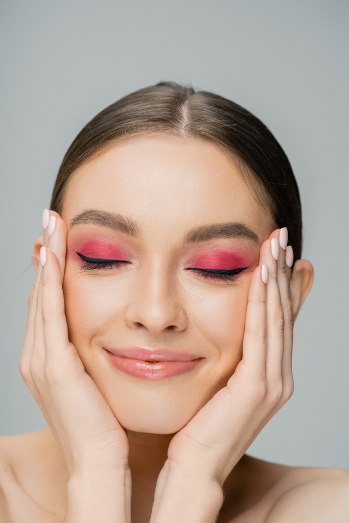 Positive woman with bright makeup touching face and closing eyes isolated on grey  - Fotoğraf, Görsel
