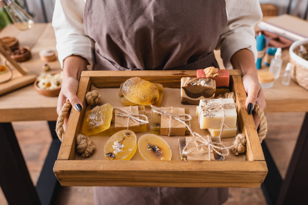 wooden tray with assortment of handmade soap in hands of cropped african american craftswoman  - Foto, immagini
