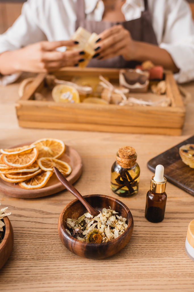 dried herbs and orange slices near essential oils and cropped african american craftswoman on blurred background - Foto, Imagen